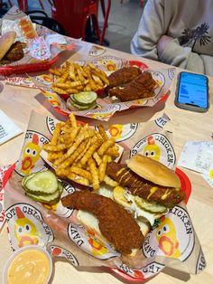 two trays filled with sandwiches and fries next to a cell phone on a table