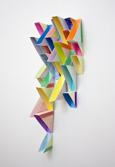 an art piece made out of colored paper on a white wall with no one around it