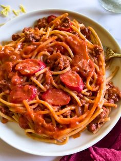 a white plate topped with spaghetti and meat covered in sauce on top of a table