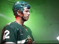 a young man wearing a green hockey uniform and helmet with the number 2 on it