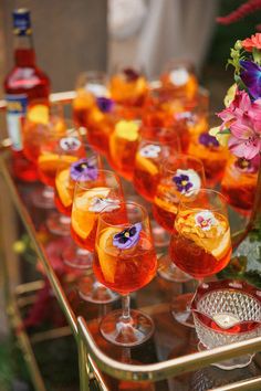 many glasses filled with different types of drinks on a metal tray next to some flowers