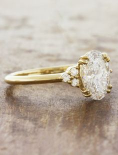 a yellow gold ring with an oval cut diamond and three smaller round diamonds on the band