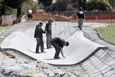 three men are standing at the top of a skateboard ramp while another man stands on one knee