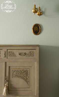 a white cabinet with an ornate design on the front and side, against a pale blue wall