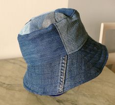 Blue jeans bucket hat. For him or her. This hat is made from upcykled blue denim. I sewn it on my lovely vintage sewingmachine. And yes, you can tell this item is handmade and quite unike.  It has a small  zipper pocket and several seams from the fabric, wich use to be trousers. The top of this hat is made from small patches. Inside has a cord in a canal in the lining Inside lining is from light lilac cotton. You can wash in machine, 40 celicius and iron the brim. The brim is sturdy enough to be a good sunscren, and soft enough to sleep comfy on the bus. This hat is a medium size, about 57-58 cm/22,8-23 inch, and it is totaly unike, like you! It is handmade by me, and labeled "carrot". The carrot label is for things I sew from upcykled fabrics, and stands for eco-friendly items.  It will b Dark Wash Denim Bucket Hat, Denim Blue Cotton Bucket Hat With Curved Brim, Denim Blue Bucket Hat With Short Brim, Denim Blue Bucket Hat, Denim Bucket Hat In Medium Wash, Denim Bucket Hat, One Size Fits Most, Blue Denim Bucket Hat With Short Brim, Brimmed Denim Blue Bucket Hat, Blue Denim Bucket Hat