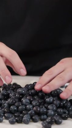 two hands reaching for blueberries on a plate