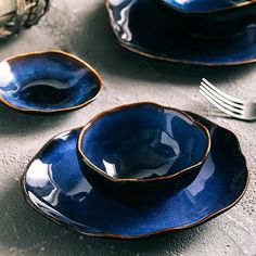 blue dishes with gold rims and silverware on a gray tablecloth next to utensils