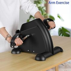 a woman is using an arm exercise device on a table with a plant in the background