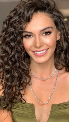 a woman with long curly hair wearing a green dress and smiling at the camera while holding a cell phone in her hand