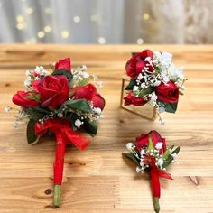 three red roses and baby's breath boutions on a wooden table next to a mirror