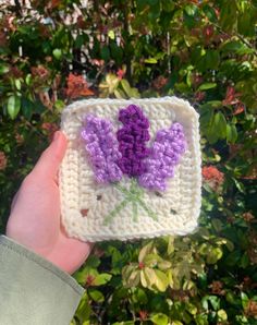 someone is holding up a crocheted square with flowers on it