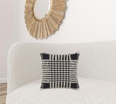 a white couch with a black and white checkered pillow on it next to a round mirror