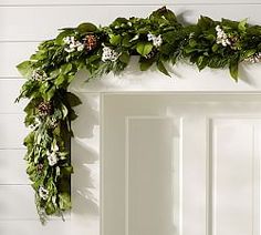 a white door decorated with greenery and flowers on the front of it, next to a wreath