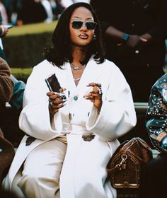 a woman sitting on a bench holding two cell phones in her hands and looking at the camera