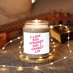 a candle that is sitting on a table with some string lights and a guitar in the background