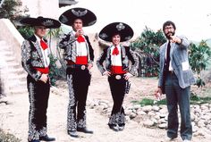 three men dressed in mexican style clothing posing for the camera with one pointing at the camera