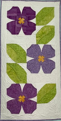 a quilted wall hanging with purple flowers and green leaves on the bottom half of it