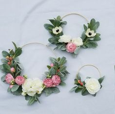 three hoop wreaths with flowers and greenery on white fabric background, top view