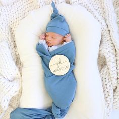 a baby wrapped in a blue blanket laying on top of a white pillow with a name tag