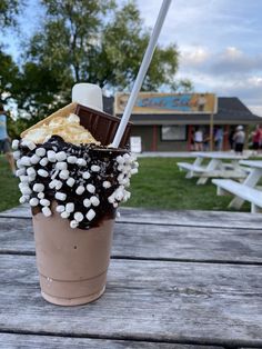 an ice cream sundae with marshmallows and chocolate on the top is sitting on a picnic table