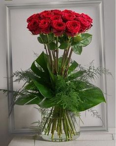 a vase filled with red roses sitting on top of a white table next to a framed photo