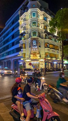 two people on a pink scooter in front of a large building at night