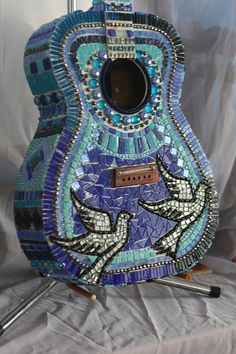 a blue and green mosaic guitar sitting on top of a white cloth covered tablecloth