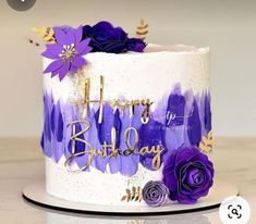 a white and purple cake with flowers on it's side that says happy birthday