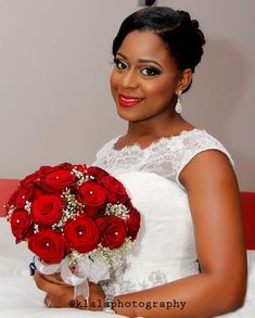 a woman in a wedding dress holding a bouquet of red roses and smiling at the camera