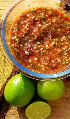 a glass bowl filled with salsa next to limes