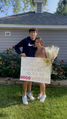 two people standing in front of a house holding a sign