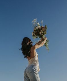 a woman holding flowers in the air with her back to the camera, against a blue sky