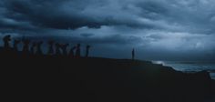 a group of people standing on top of a cliff near the ocean under a cloudy sky