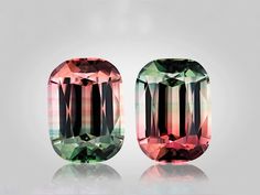 two different colored gems sitting next to each other on a white surface and one is green, the other is pink