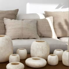 white vases and pillows on a wooden table in front of a couch with cushions