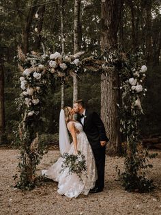 a bride and groom kissing under an arch decorated with flowers