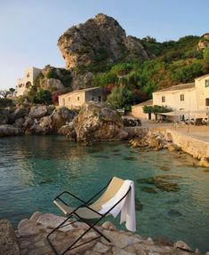 a chair sitting on the edge of a body of water next to a rocky cliff