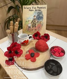 a wooden table topped with red flowers next to a greeting card and two bowls filled with candy