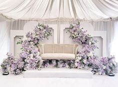 a white couch sitting under a canopy covered in purple and white floral arrangements on top of a stage