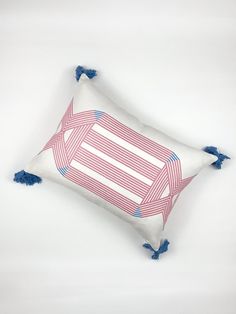 a white pillow with blue tassels and a pink striped design on it, sitting on a white surface