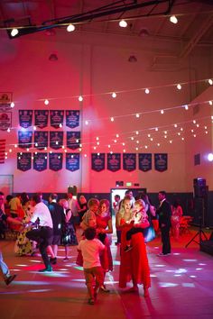 people are dancing in a large room with lights strung from the ceiling and posters on the walls