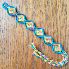 a colorful braided bracelet sitting on top of a wooden table next to a piece of string