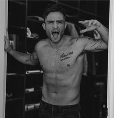 a shirtless man with his arms spread wide open in front of a mirror, making the middle finger sign