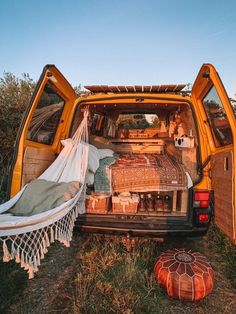 the back end of an orange van filled with luggage and blankets, sitting in a field