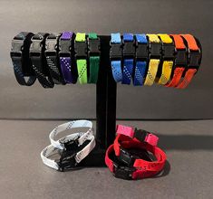 four different colored wristbands on a black metal stand against a gray background,