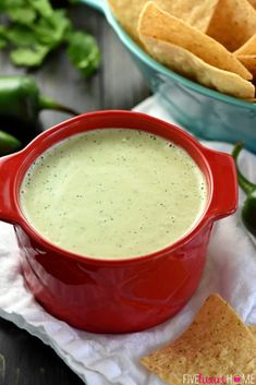 a red pot filled with green sauce next to tortilla chips on a napkin