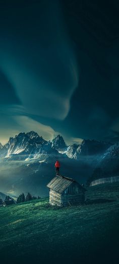 a person standing on top of a building in the middle of a field with mountains