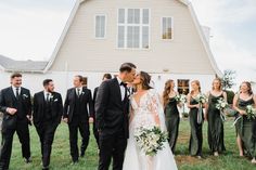 a bride and groom kissing in front of their wedding party on the lawn at a farm