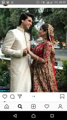 two people standing next to each other in front of trees and bushes, one is wearing a wedding dress