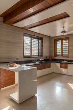 an empty kitchen with white counter tops and wooden ceilinging, along with large windows